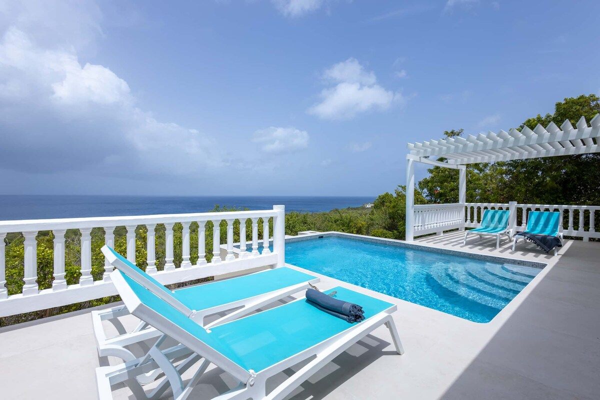 A poolside area with lounge chairs and a pergola overlooking a body of water.