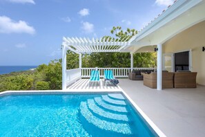 A swimming pool with a white pergola and lounge chairs, overlooking a scenic view.