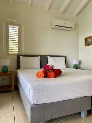 A neatly made bed with white linens, two pillows, and a decorative flower arrangement.
