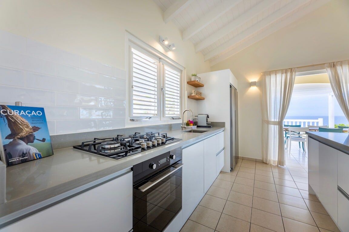 A modern kitchen with a gas stove, oven, and white cabinetry. There is a window with blinds, a countertop with a sink, and a view of the outdoors.