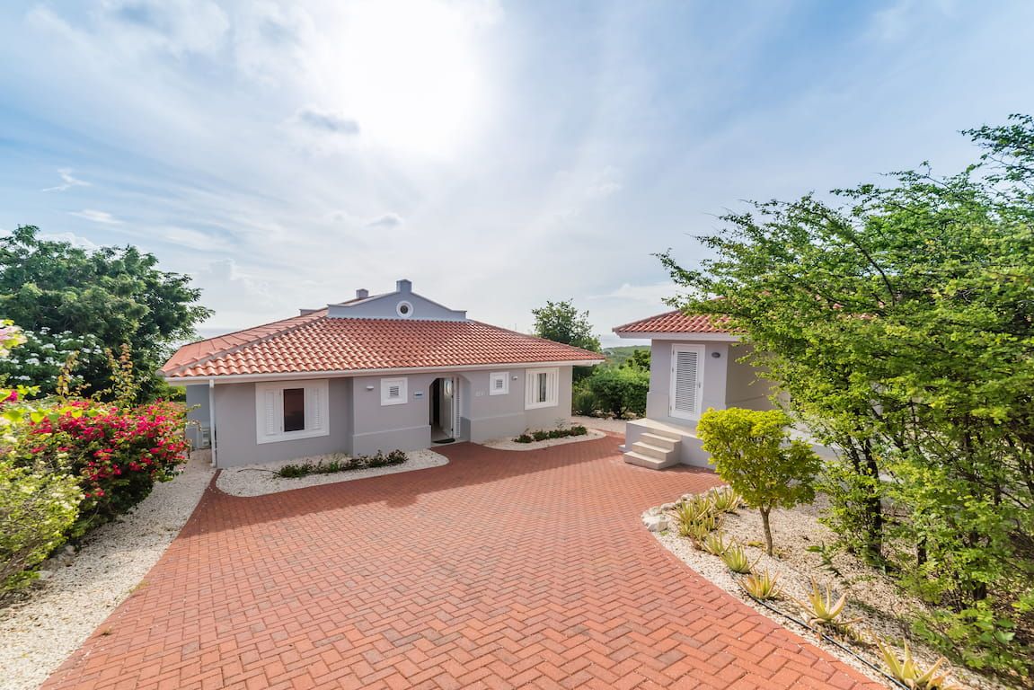 Ein zweistöckiges Haus mit rotem Ziegeldach, einer Pflasterauffahrt und einem kleinen Garten mit verschiedenen Pflanzen und Blumen.