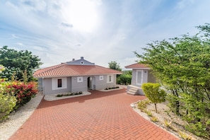 Ein zweistöckiges Haus mit rotem Ziegeldach, einer Pflasterauffahrt und einem kleinen Garten mit verschiedenen Pflanzen und Blumen.