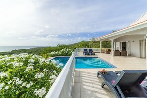 Ein Poolbereich mit Liegestühlen, einer überdachten Terrasse und Blick auf das Meer.