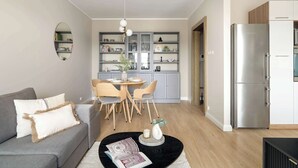 A modern living room with a grey sofa, a black coffee table, and a dining area with a wooden table and chairs. A kitchen with grey cabinets and a stainless steel refrigerator is visible in the background. - Comfortable Apartment in Poznan | Garage | Balcony (Poznań)