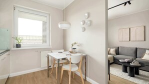 A modern living room with a grey sofa, a coffee table, and a dining area with a white table and wooden chairs. - Comfortable Apartment in Poznan | Garage | Balcony (Poznań)
