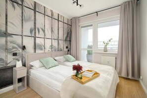 A modern bedroom with a large bed, a bedside table, a window with curtains, and a view of the outdoors. - Comfortable Apartment in Poznan | Garage | Balcony (Poznań)