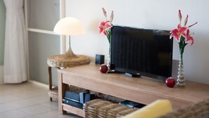 Una sala de estar con un mueble de madera para entretenimiento, un televisor, una lámpara y dos jarrones con flores.