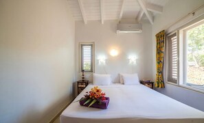 A hotel room with a large bed, two bedside lamps, a window with curtains, and an air conditioning unit. - Cosy villa with privacy and panoramic sea views (Sint Willibrordus)