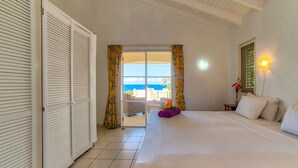 Habitación de hotel con una cama, una mesita de noche, una lámpara, vista al océano y una puerta corrediza que da a un balcón.