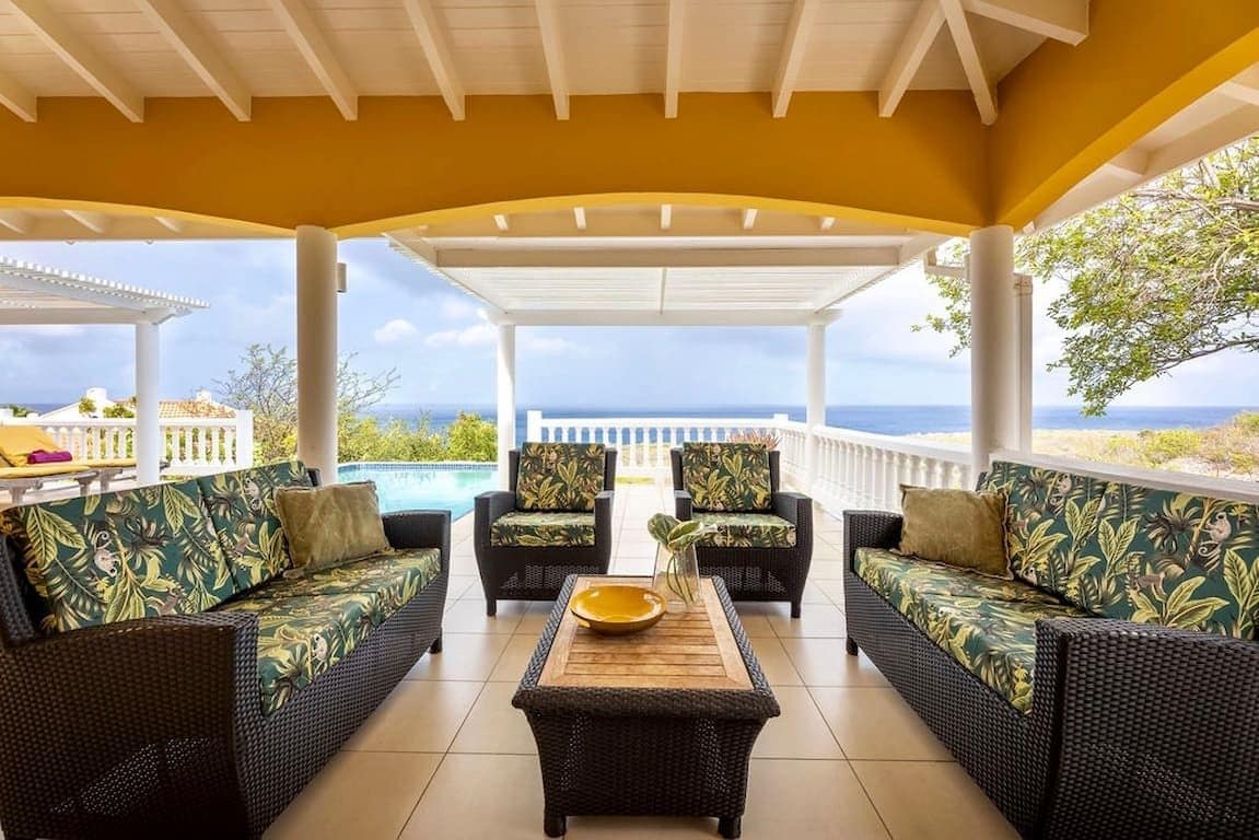 A covered outdoor seating area with wicker furniture and a view of the ocean.