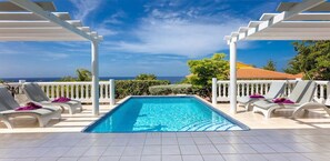 Zona de piscina amb vista despejada a l'oceà, pèrgola blanca i gandules.