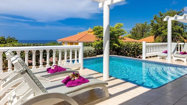A poolside area with white pergola, lounge chairs, and a clear view of the ocean. - Elegant sea-view villa with private pool - Coral Estate (Sint Willibrordus)