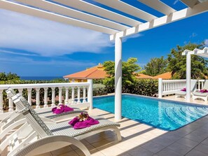 A poolside area with white pergola, lounge chairs, and a clear view of the ocean. - Elegant sea-view villa with private pool - Coral Estate (Sint Willibrordus)