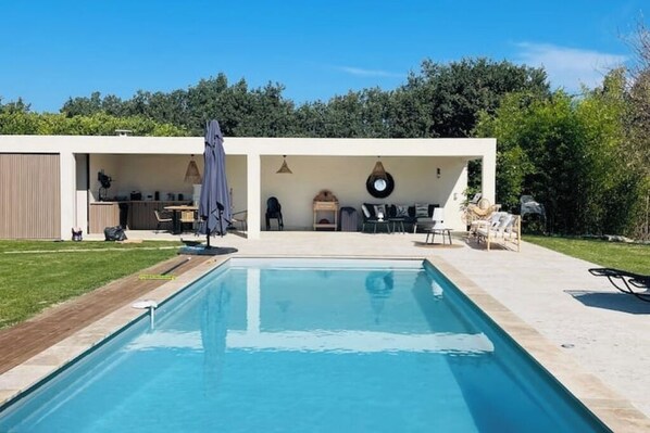 A rectangular pool with a tiled deck, surrounded by a covered patio area with outdoor furniture.