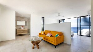 Una sala de estar moderna con un sofá, una mesa de centro de vidrio y vista al mar a través de ventanas amplias.