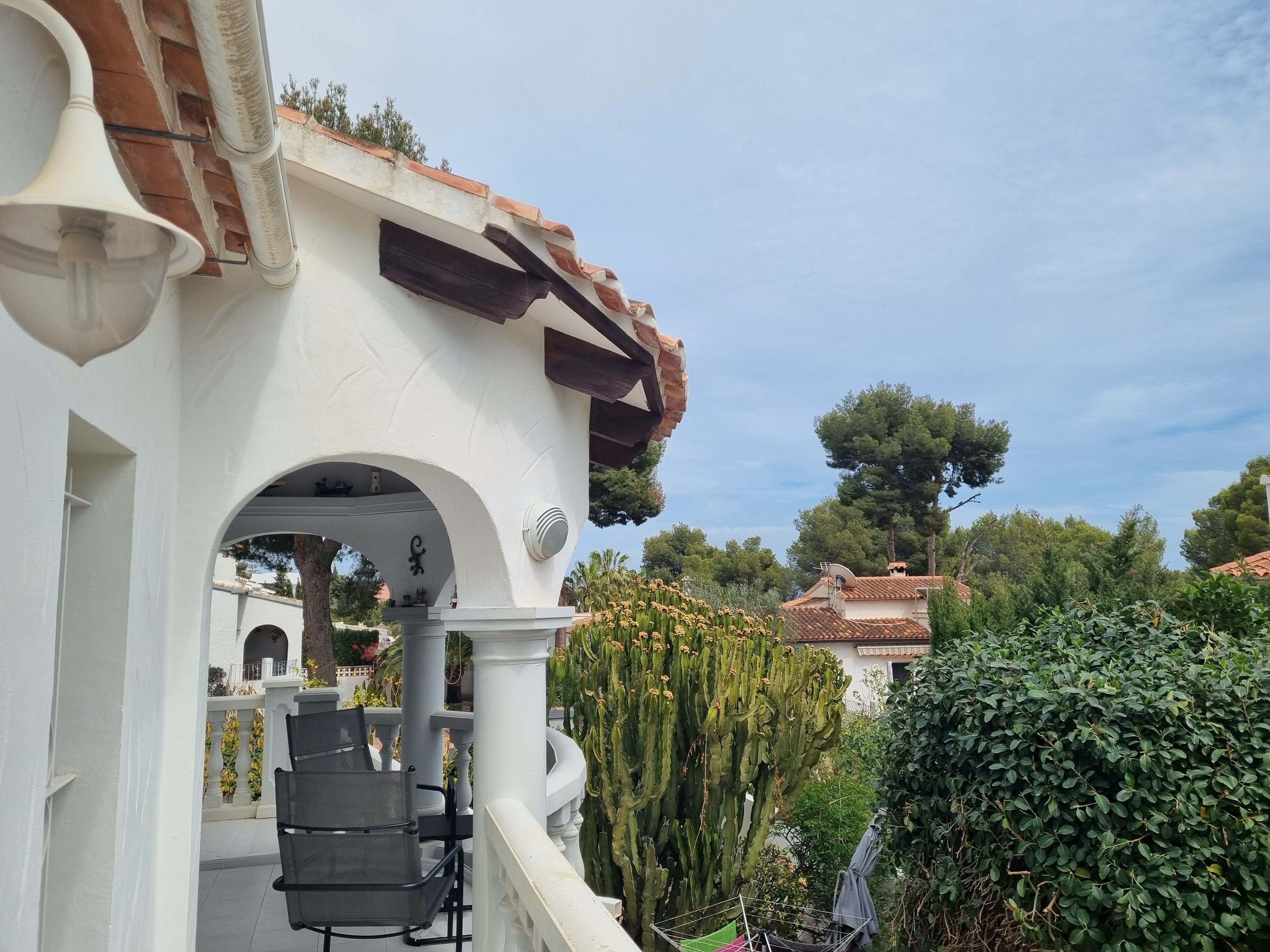 A white building with a tiled roof and a balcony with outdoor furniture.