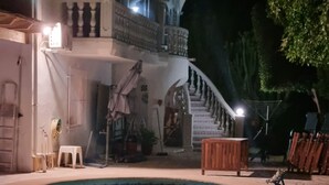 Une piscine à bordures courbes, un escalier menant à un balcon et un bâtiment blanc doté d’un balcon et d’une balustrade.