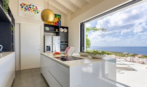 A modern kitchen with a large window, a view of the sea, and a dining area with a view. - Modern sea-view villa with private infinity pool (Sint Willibrordus)