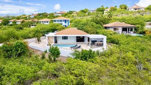 A residential area with houses surrounded by lush greenery, a swimming pool, and a clear sky. - Tropical hideaway with private pool and ocean view (Sint Willibrordus)
