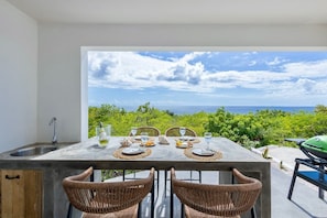A dining area with a view of the sea, a grill, and wicker chairs. - Tropical hideaway with private pool and ocean view (Sint Willibrordus)