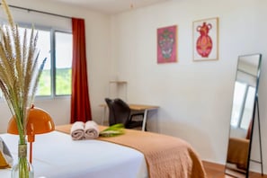A hotel room with a bed, a desk, a chair, a mirror, and artwork on the wall. - Tropical hideaway with private pool and ocean view (Sint Willibrordus)