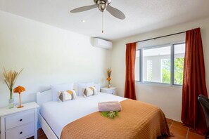 Een hotelkamer met een bed, nachtkastje, lamp, plafondventilator, airconditioning en een raam met gordijnen.