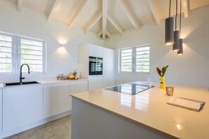 A modern kitchen with white cabinetry, a central island, and pendant lighting. - Romantic garden bungalow with pool and sea view (Sint Willibrordus)