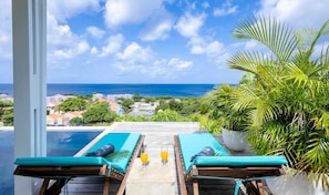 A poolside area with lounge chairs and a view of the ocean. - Romantic garden bungalow with pool and sea view (Sint Willibrordus)