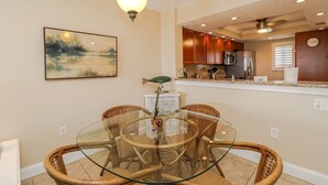 Un comedor con sillas de mimbre y una mesa de vidrio, una cocina con armarios de madera y un cuadro en la pared.