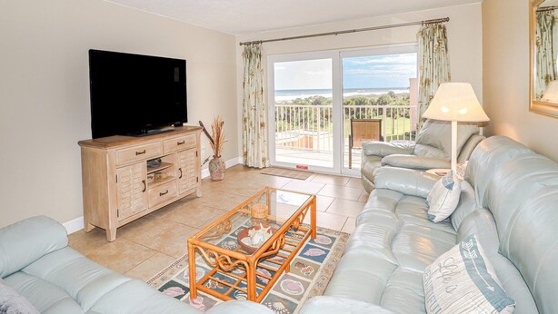 Una sala de estar con sofá, mesa de centro, televisor y balcón con vistas.