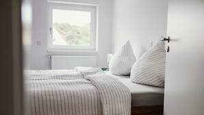 A bedroom with a bed, pillows, a window, and a radiator.