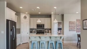 Une cuisine moderne avec des meubles blancs, des appareils en acier inoxydable et un îlot central doté de tabourets de bar.