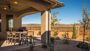 Une terrasse couverte avec une table et des chaises, un barbecue et une vue sur un paysage désertique.