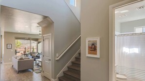 Un intérieur de maison moderne comprenant un escalier, un salon avec un canapé et une table basse, et une salle de bain avec des toilettes et un rideau de douche.