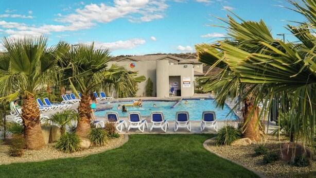 Un espace piscine avec des chaises longues, des palmiers et un bâtiment portant une enseigne.