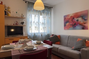 Un salon avec un canapé, une table à manger dressée avec des assiettes et des couverts, un téléviseur et un tableau accroché au mur.