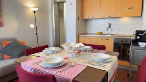 Ein Essbereich mit Tisch für vier Personen, eine Küche mit Herd und Backofen sowie ein roter Stuhl.