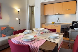 A dining area with a table set for four, a kitchen with a stove and oven, and a red chair.