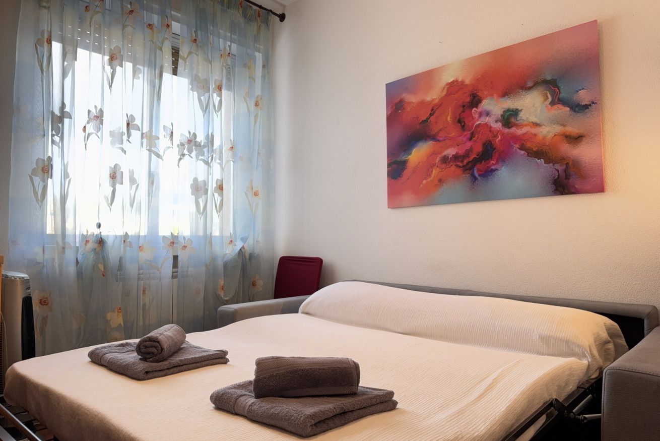 Ein Hotelzimmer mit einem Bett, einem roten Sessel, einem Bild an der Wand und einem Fenster mit floralem Vorhang.