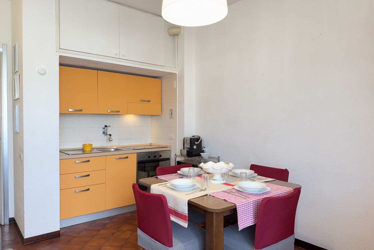 A compact kitchen with a dining table set for four, featuring a checkered tablecloth and red chairs.