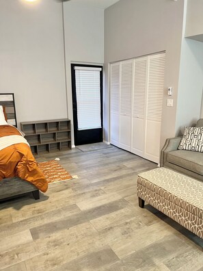 Ein modernes Schlafzimmer mit einem Bett, einem Schlafsofa, einem gemusterten Hocker, einer integrierten Bank und einem Kleiderschrank.