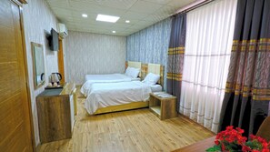Ein Hotelzimmer mit zwei Betten, Holzboden, Spiegel, Fernseher und Vorhängen.