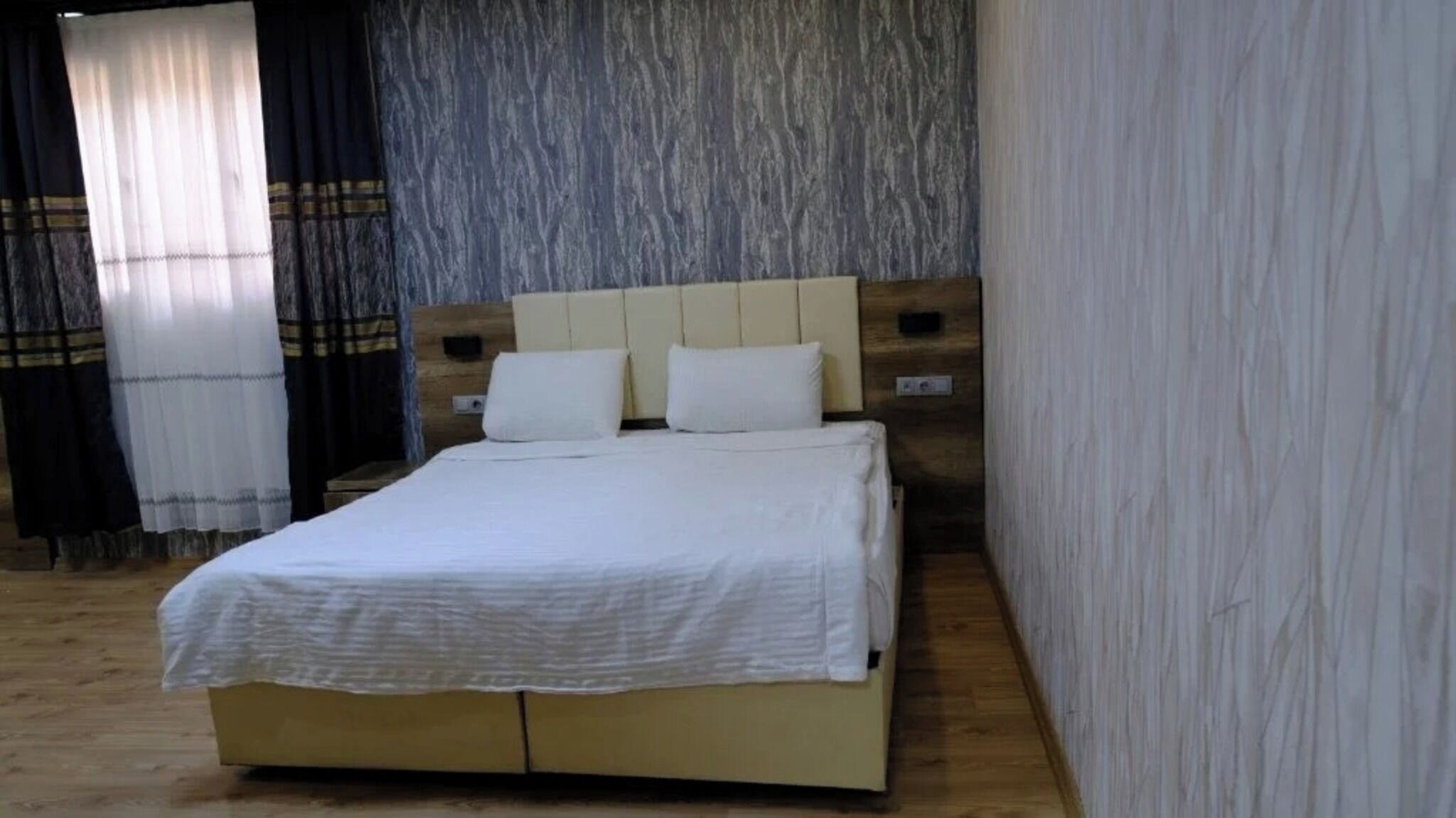 Una cama bien hecha en una habitación con piso de madera y pared con textura.