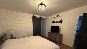 Un dormitorio con una cama grande, un aparador, un televisor y un adhesivo mural de montañas.
