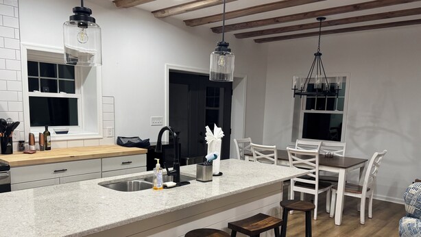 Una cocina moderna con una isla central, taburetes de bar y un comedor con sillas blancas.