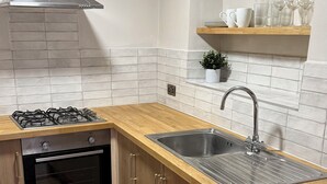 Eine moderne Küche mit Gasherd, Backofen, Spüle aus Edelstahl und Holzschränken.