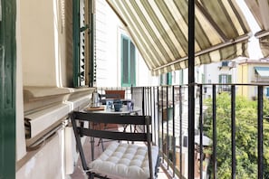 A balcony with a cushioned chair, a small table with a kettle, and a view of the street below. - Spartaco Prestigious Apartment (Firenze)