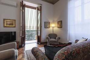 A room with a television, a patterned sofa, a chair, and a lamp. - Spartaco Prestigious Apartment (Firenze)