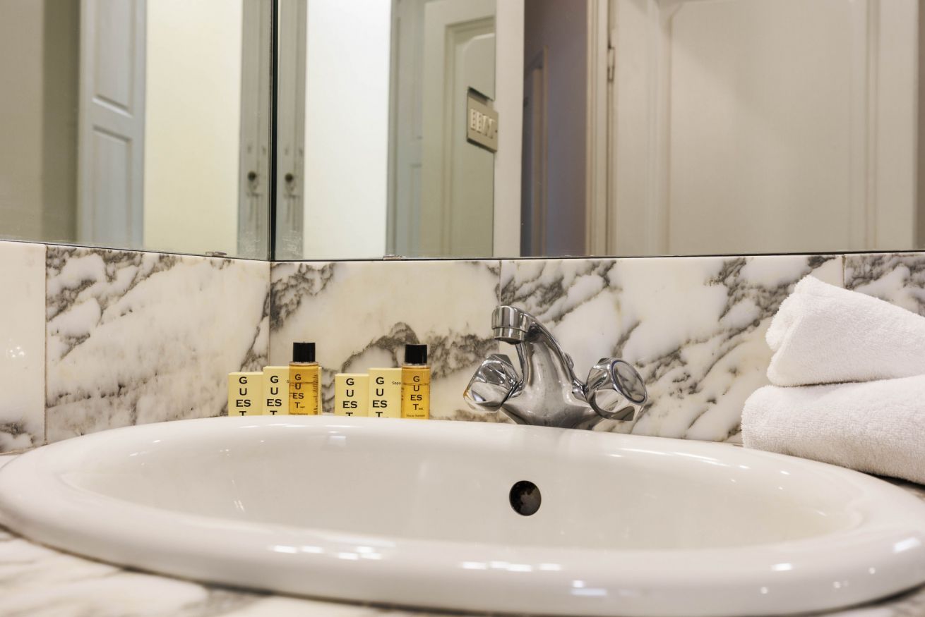 Un baño con lavamanos de mármol, espejo y artículos de aseo.
