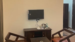 Ein Zimmer mit einem an der Wand befestigten Flachbildfernseher, einem Holztisch, zwei Holzstühlen und einer Klimaanlage über dem Tisch.
